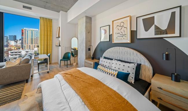 a bedroom with a large bed a side table with a lamp and frames on the wall